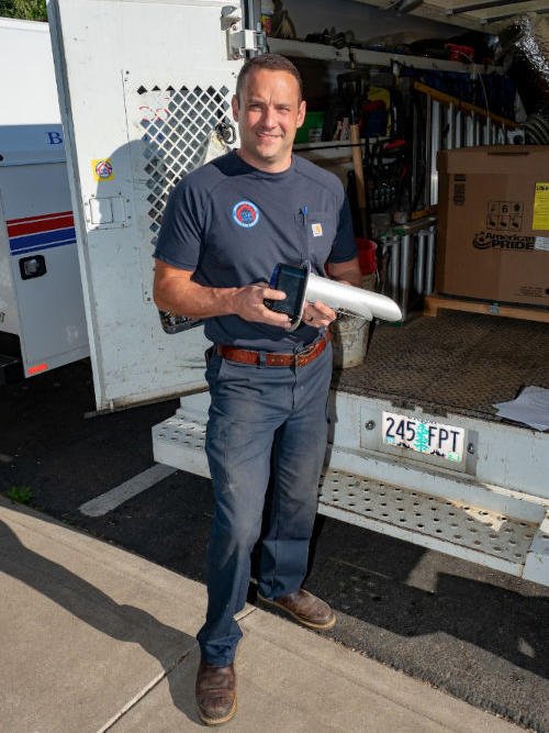 Uniformed Four Seasons tech standing at the back of his opened service vehicle, holding a unit part