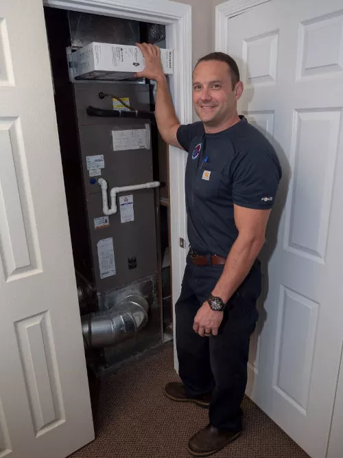 Smiling Four Seasons HVAC technician replacing an air filter