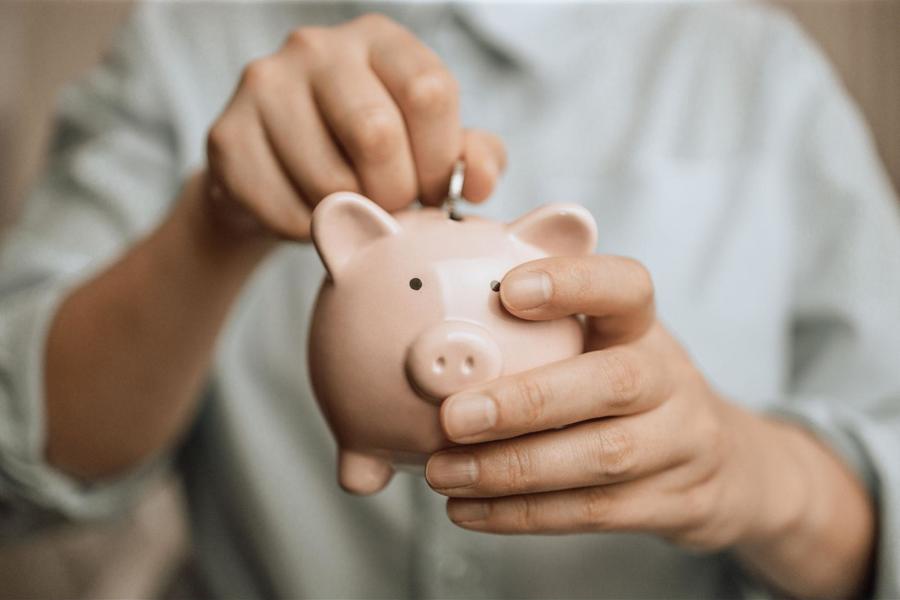 Man holding a small light pink piggy bank, placing a nickel into its top slot.