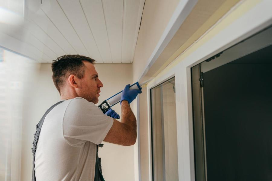 Man wearing overalls and a white shirt, applying caulk to an outdoor door