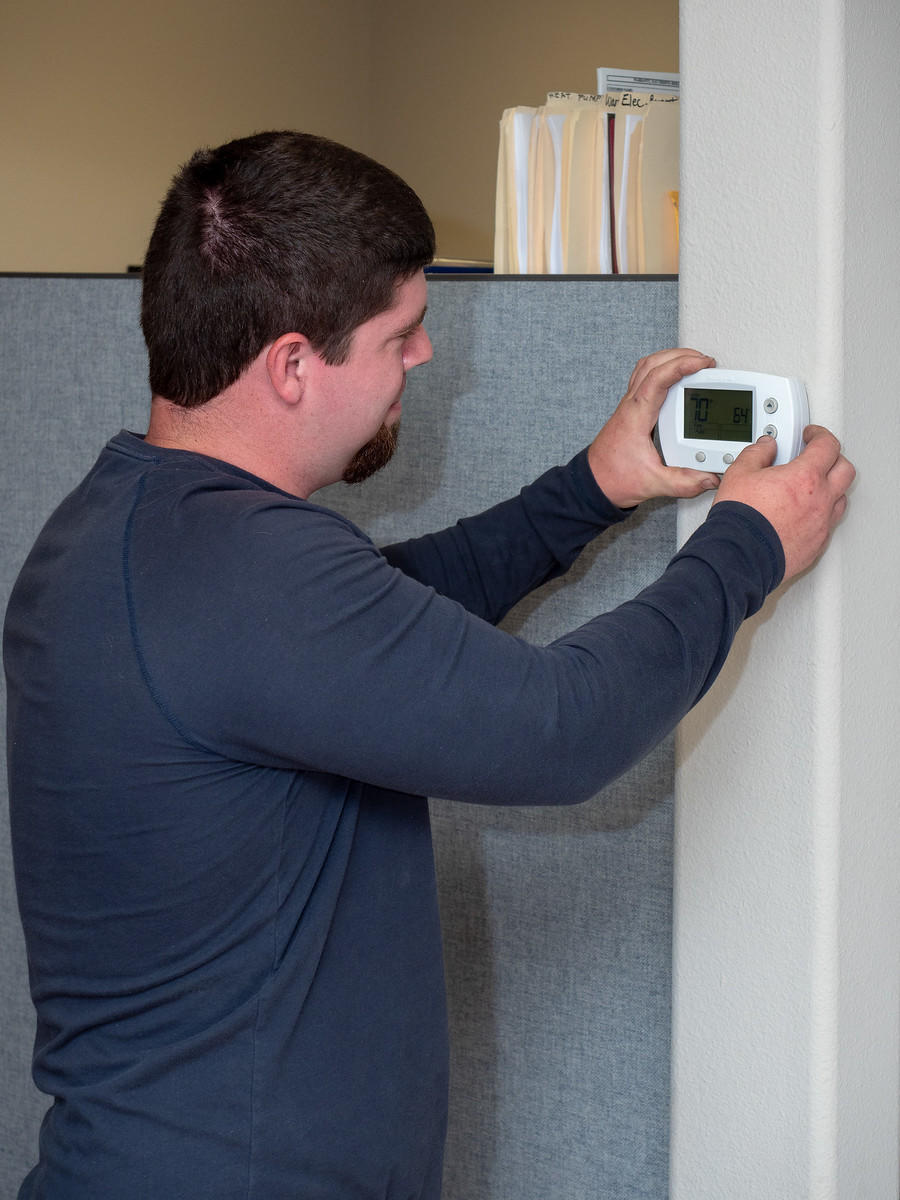 Four Seasons HVAC technician examining a thermostat