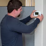 Four Seasons HVAC technician examining a thermostat