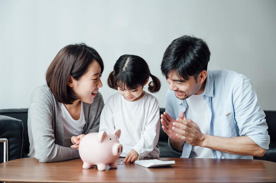 Parents teaching their daughter to save money in her piggy bank