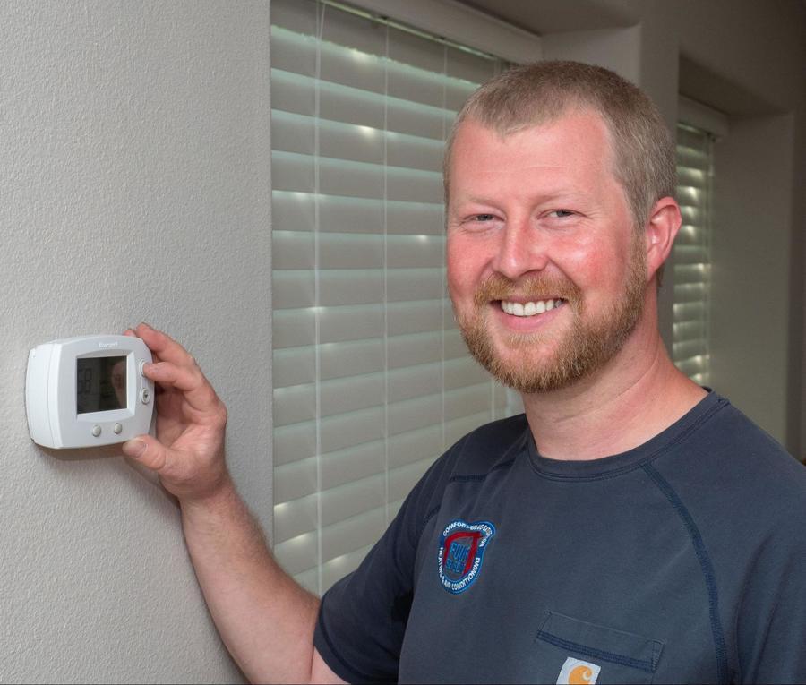 Four Seasons HVAC technician adjusting a thermostat while smiling at the camera