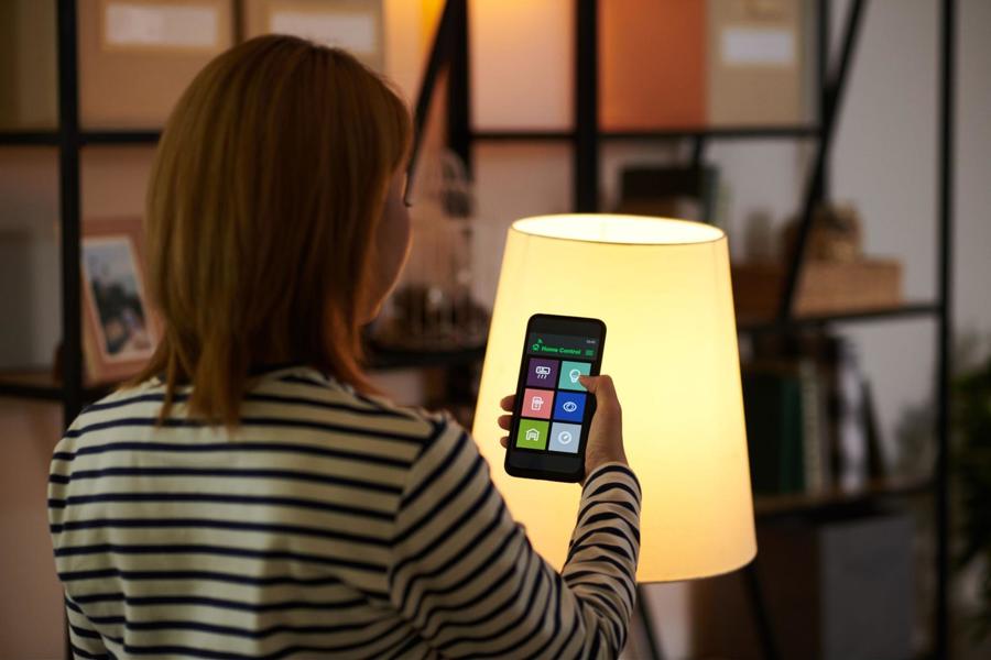 Woman facing away from the camera, wearing a striped black and white shirt, using her smartphone app to dim a living room lamp
