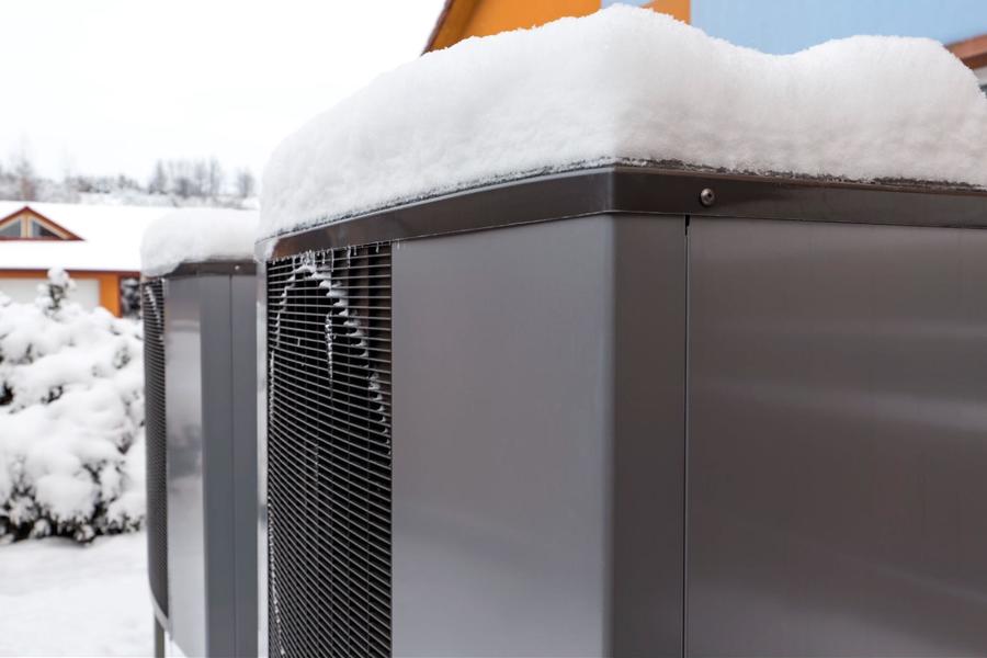 A close up of two side by side ac units, sitting atop a snow covered with a layer of snow sitting on top of each unit.