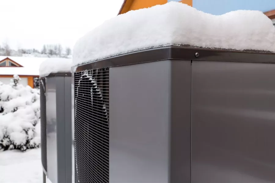 A close up of two side by side ac units, sitting atop a snow covered with a layer of snow sitting on top of each unit.