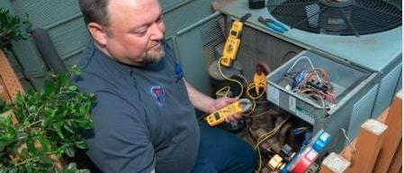 HVAC Tech wearing a Four Seasons branded shirt, working on an ac unit using multiple reading tools that are connected to the unit.