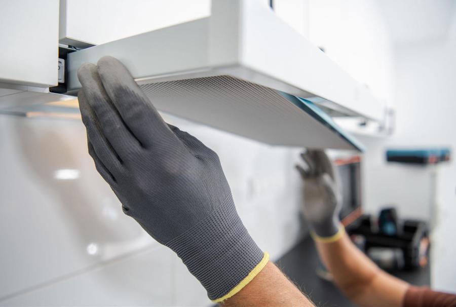 Tech wearing gray gloves changing out the ventilation screen on a stove hood.