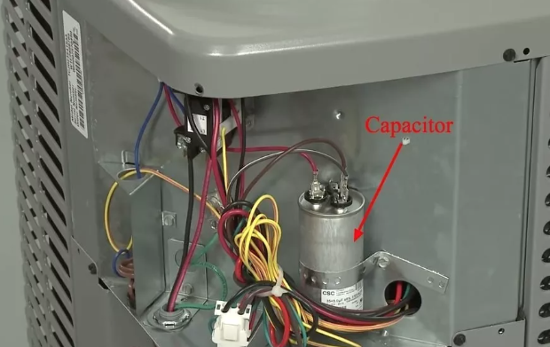 Close up photo showing the capacitor part on a heat pump that is surrounded by various exposed wiring.