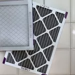 A clean square air filter laying across a clean rectangle one that is on a white tiled floor