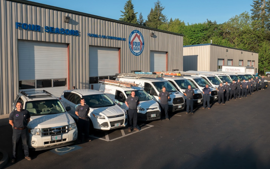 Four Seasons HVAC technicians wearing branded t-shirts standing next to service vehicles in front of their facilities