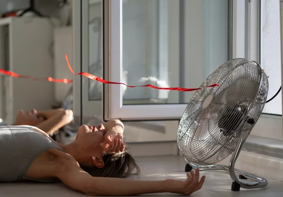 Woman laying on the floor with her arm over her forehead next to a floor fan blowing air