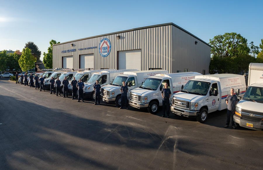 Multiple Four Seasons branded service vehicles lined up in a row alongside their warehouse facility, with 1 tech standing in front of each service vehicle.