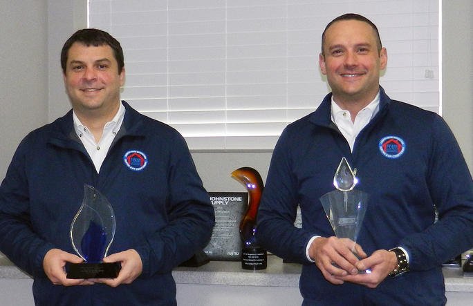 Two Four Seasons executives in branded shirts holding up awards in an office